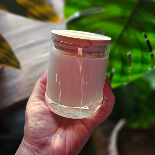 Hand holding a clear container with a pinkish liquid against a green leafy background