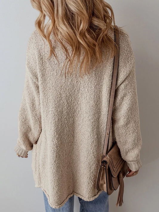 Person wearing a beige sweater and holding a brown bag against a plain background