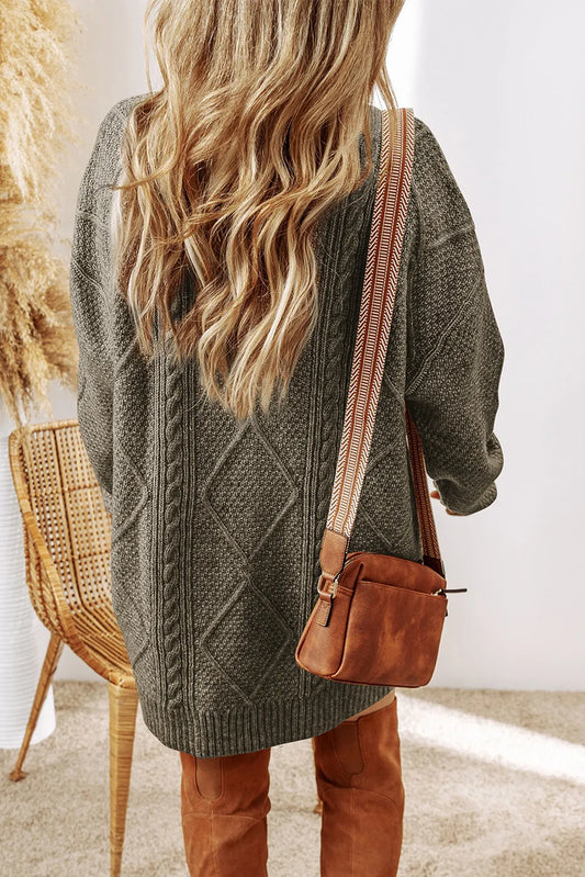 Person wearing a green cable knit sweater and brown leather pants with a brown leather bag.