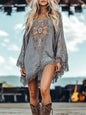Woman wearing a gray embroidered dress with fringe and cowboy boots outdoors.