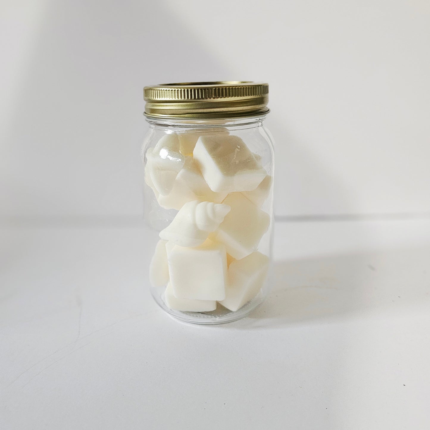 Clear glass jar with gold lid containing white cubes on a white background