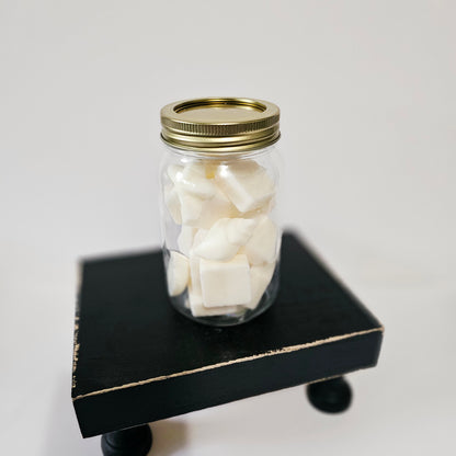 Clear glass jar with gold lid containing white cubes on a black stand against a light gray background