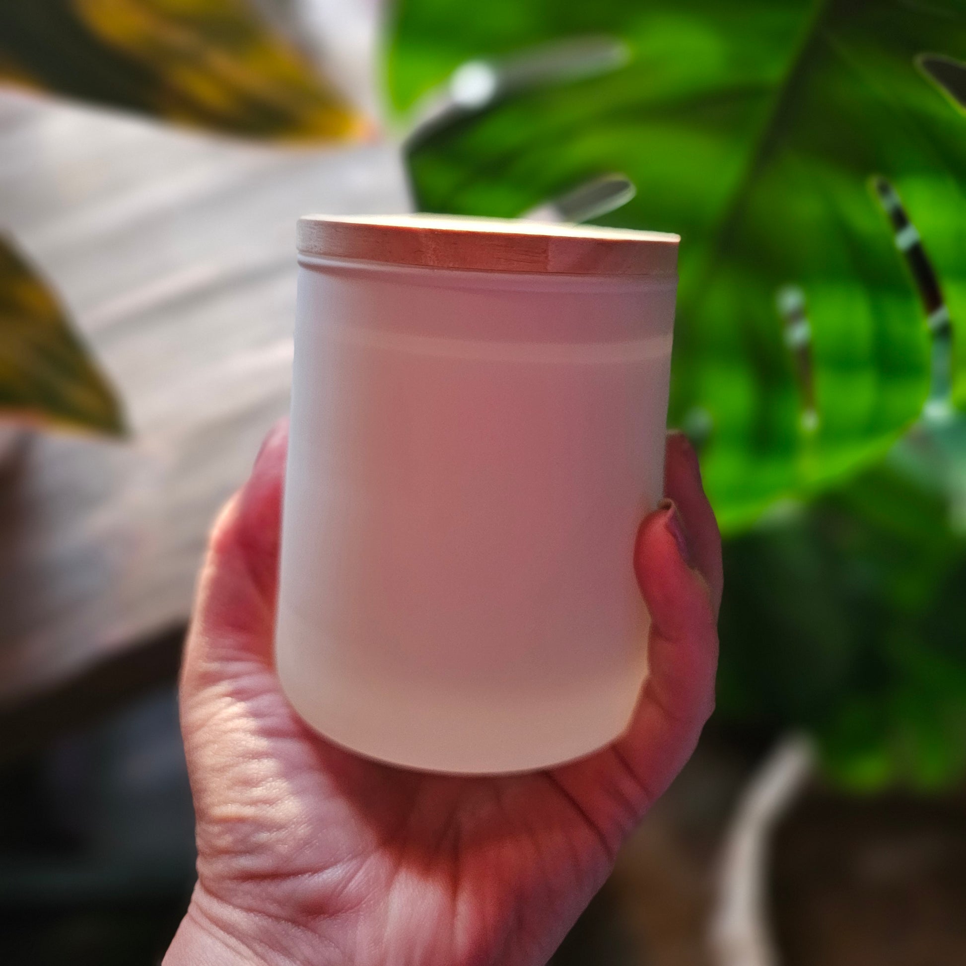 Hand holding a white cup with green plants in the background