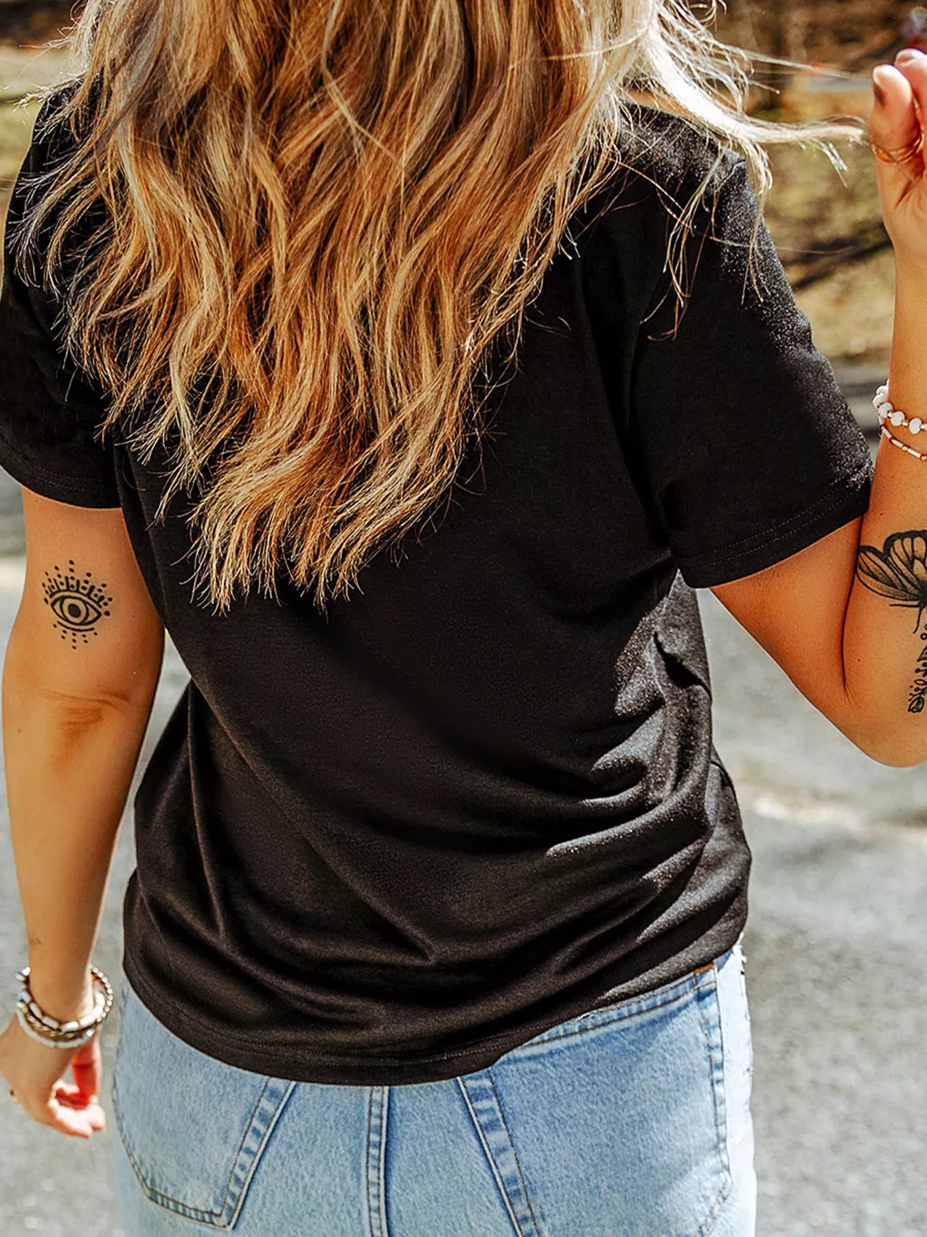 Person wearing a black t-shirt and light blue jeans with tattoos on arms.