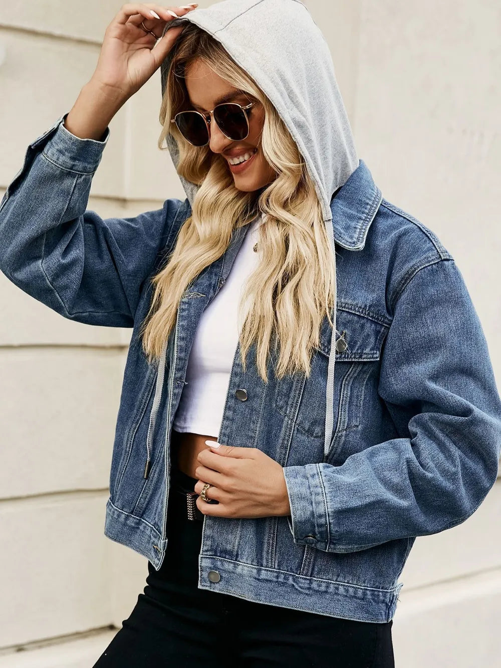 Person wearing a denim jacket with a hood, sunglasses, and a white top.