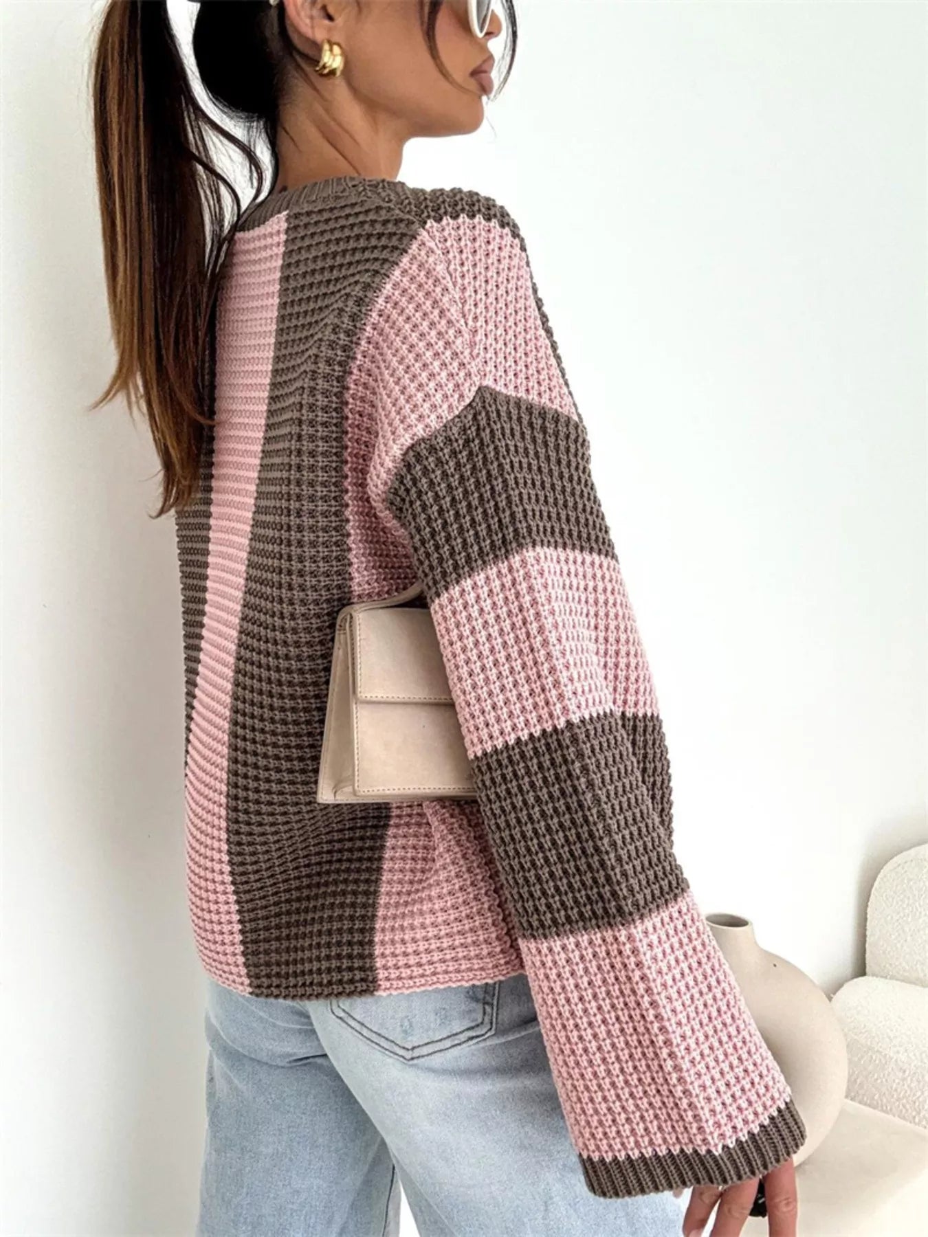 Person wearing a pink and brown striped sweater with a neutral background