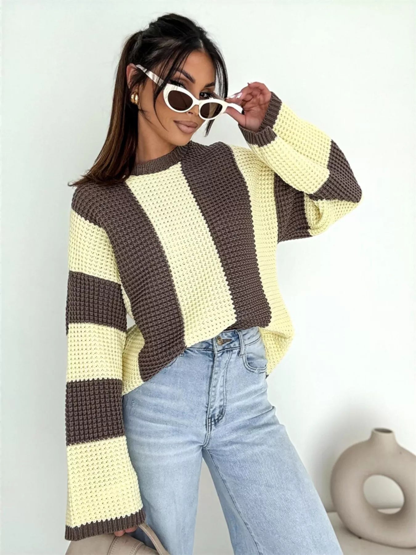 Woman wearing a striped sweater and sunglasses against a plain background