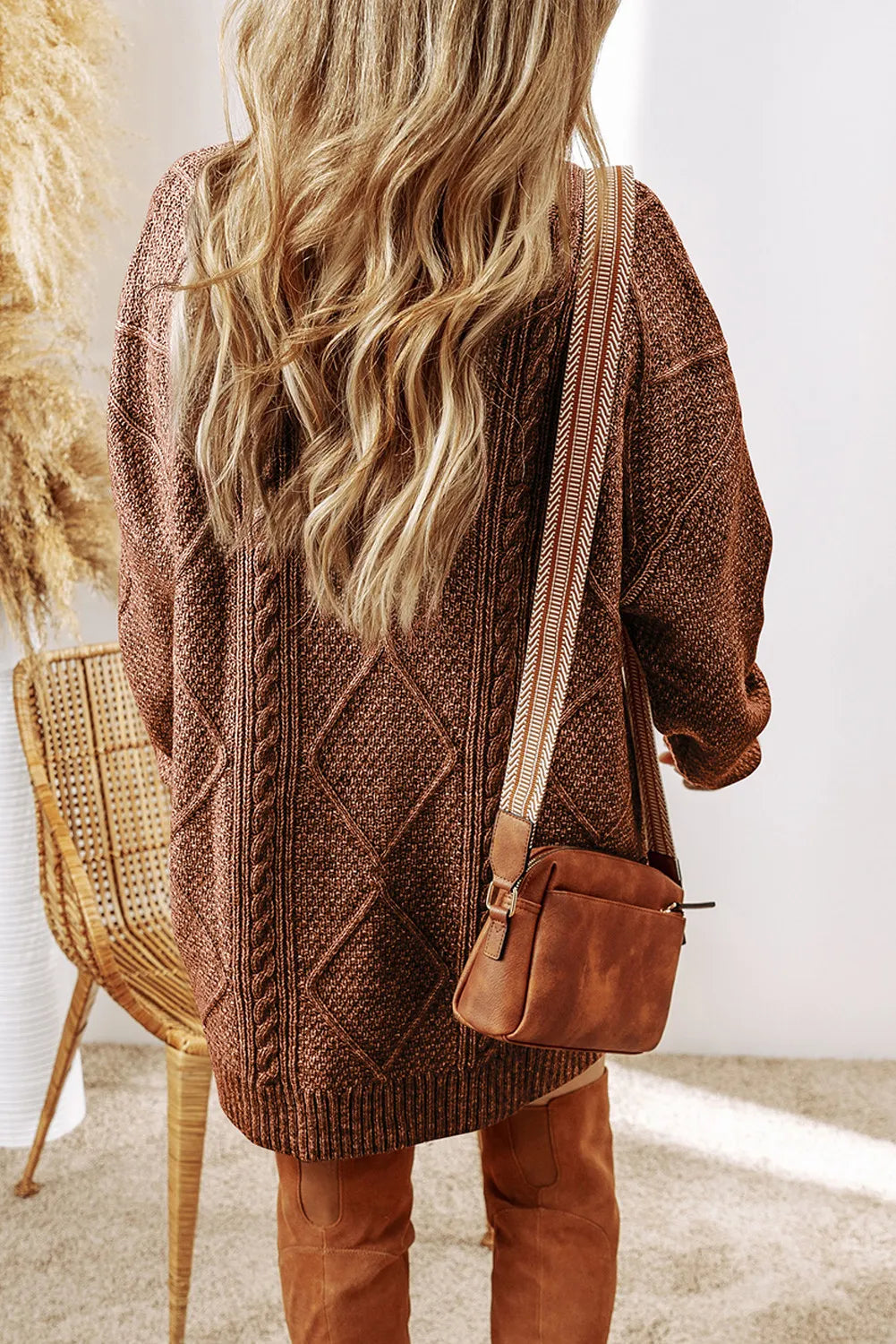 Person wearing a brown knitted cardigan and holding a brown bag indoors.