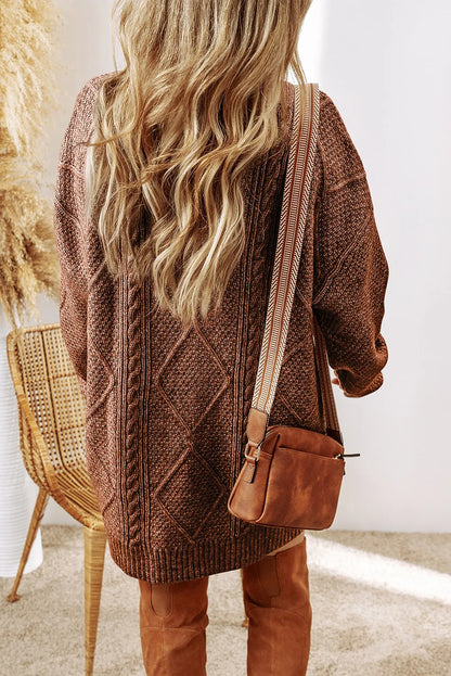 Person wearing a brown knitted cardigan and holding a brown bag indoors.