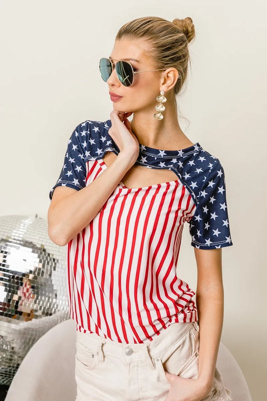 The American Flag Theme Front Cut Out Top showcases patriotic flair with its American flag theme design. The front cut-out detail adds a trendy and edgy touch to the top, showcasing the stars across the shoulders and the strips down the torso.