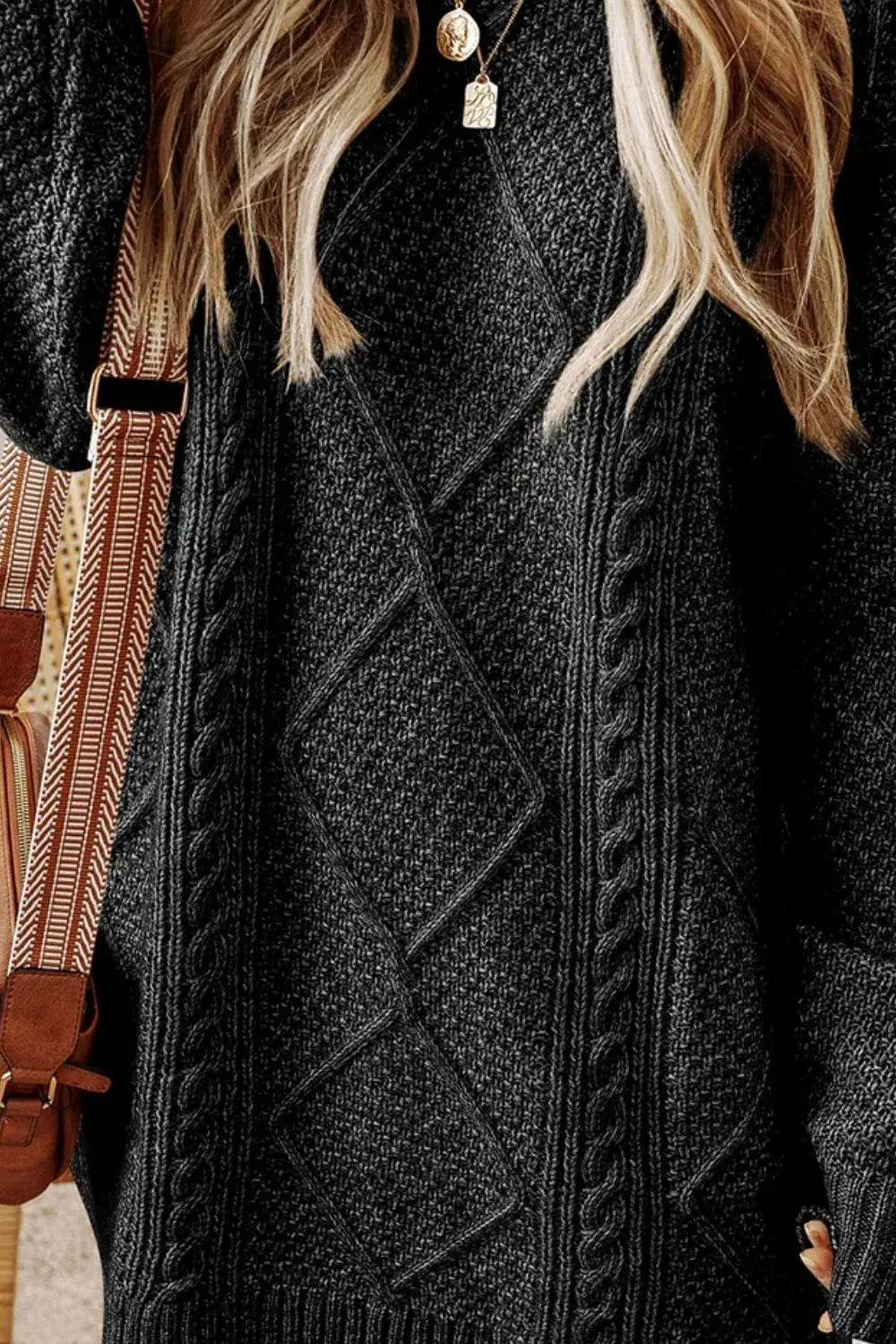 Person wearing a black cable knit sweater with a patterned bag in the background