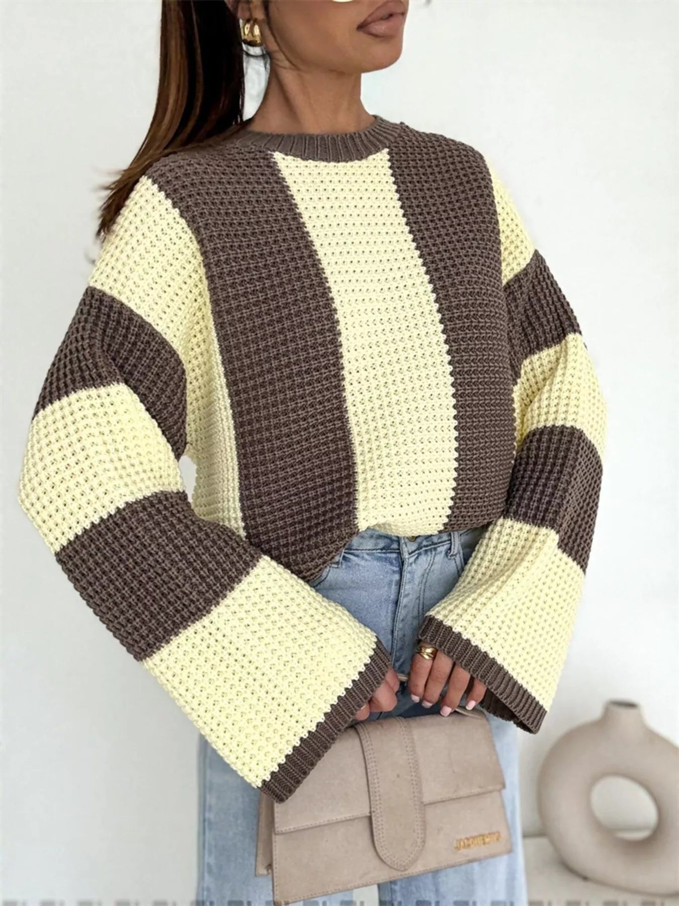 Woman wearing a striped sweater with brown and yellow colors, standing against a plain background.